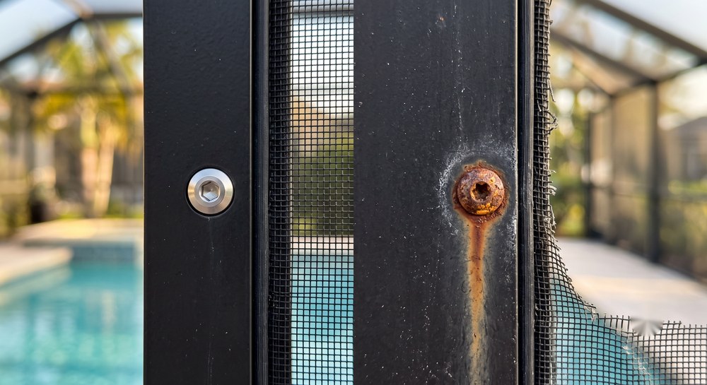 Corrosion-resistant fastener next to a rusted screw on a black aluminum pool cage frame, Sarasota FL